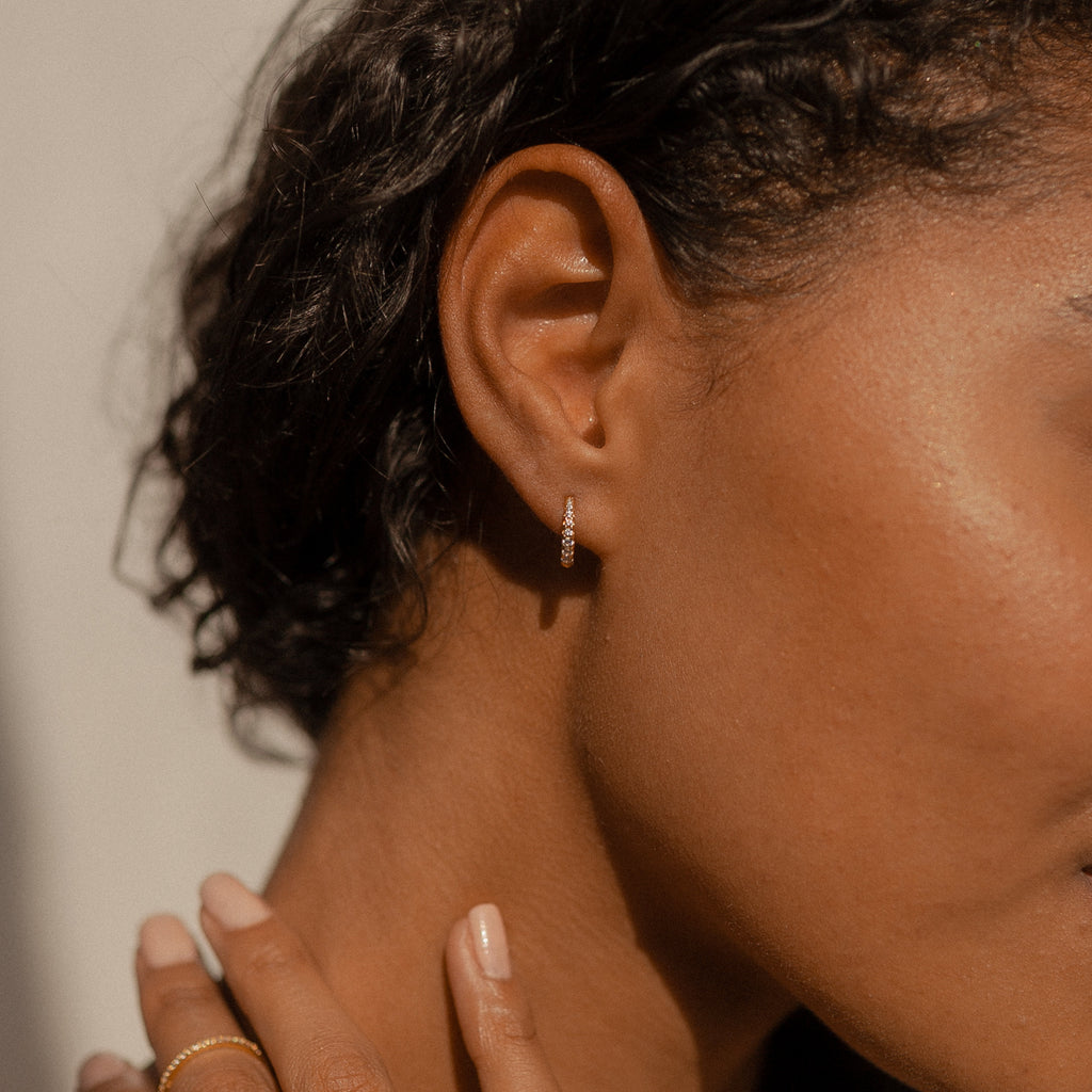 A close-up shows a woman wearing Vera Pave Huggies as she touches her neck—ideal minimalist earrings for everyday wear.