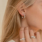 Close-up of a woman wearing Croissant Hoops with twist detailing and matching silver rings, her blonde hair falling loosely.