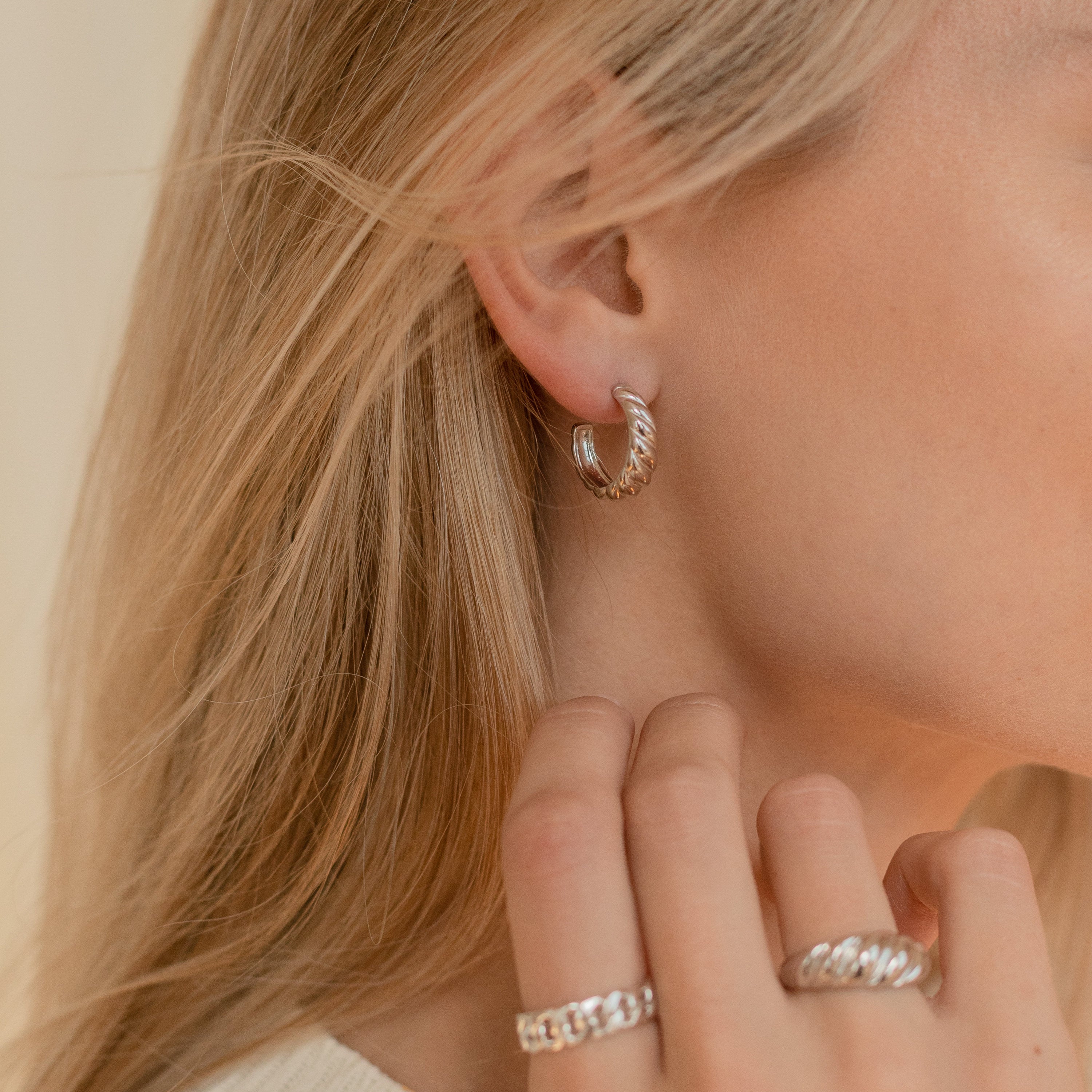 Close-up of a woman wearing Croissant Hoops with twist detailing and matching silver rings, her blonde hair falling loosely.