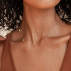 Close-up of a woman in a brown top wearing the Diamond Station Necklace, featuring delicate gold beads that highlight its modern elegance.