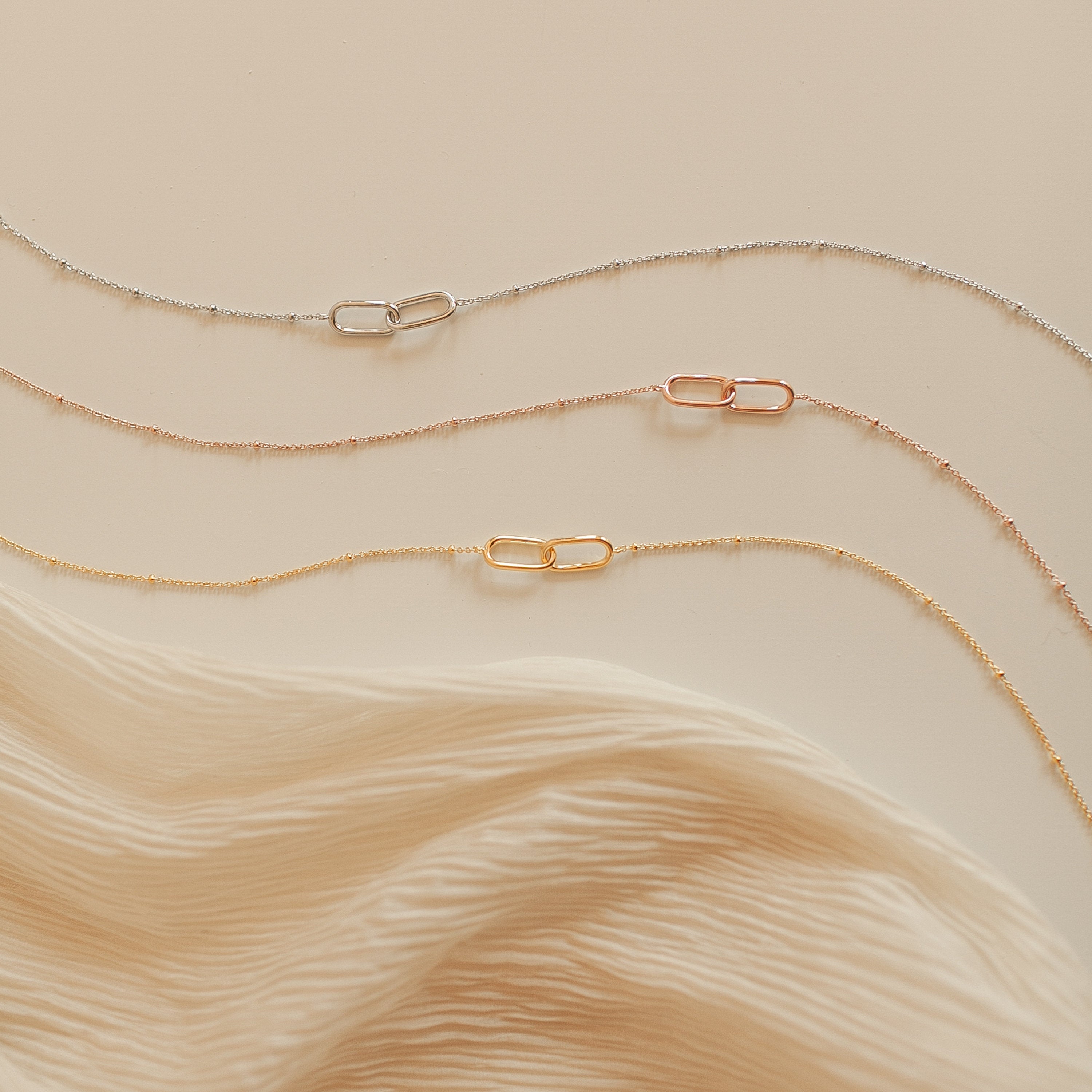 The Linked Pendant Necklace in Silver is elegantly displayed on a cream fabric background.
