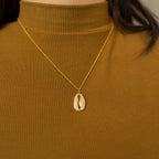 The Pave Shell Necklace on a gold chain, styled over a ribbed brown turtleneck, brings a touch of coastal cottage charm to your outfit.