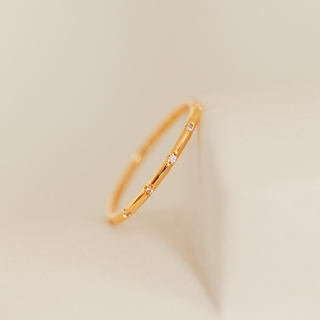 The Sprinkle Diamond Ring features small, evenly spaced diamonds on a thin gold band, shown against a soft beige background—ideal for stacking with other stackable rings.