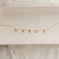 The Pave Letter Necklace features dangling letter charms spelling GRACE, shown on a white ceramic tray—a meaningful necklace and an ideal choice for personalized jewelry.