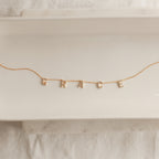 The Pave Letter Necklace features dangling letter charms spelling GRACE, shown on a white ceramic tray—a meaningful necklace and an ideal choice for personalized jewelry.
