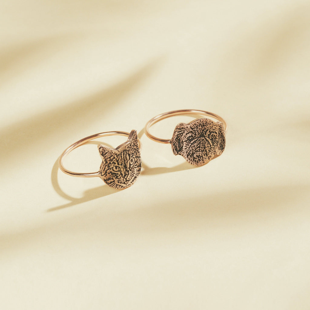 The Pet Portrait Ring features engraved cat and dog faces on a cream-colored background—ideal custom jewelry for animal lovers.