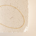 Essential Bracelet Chains with a polished gold finish are displayed on a textured, light-colored stone surface.