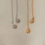 Pair these star-shaped pendant necklaces—one silver, one gold—displayed on a textured beige surface with our Lux Threader Earrings for an elegant look.