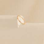 The Sprinkle Diamond Ring, ideal for stacking with other rings, is displayed on a soft beige surface with gentle light and shadow.