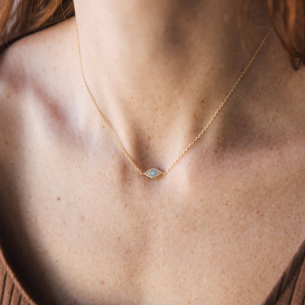 The Opal Eye Necklace features a delicate gold chain and a small oval pendant that rests gracefully on the neck.