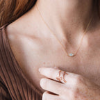 A woman wearing the Opal Eye Necklace with a small eye pendant and a 925 sterling silver forever family ring on her finger.