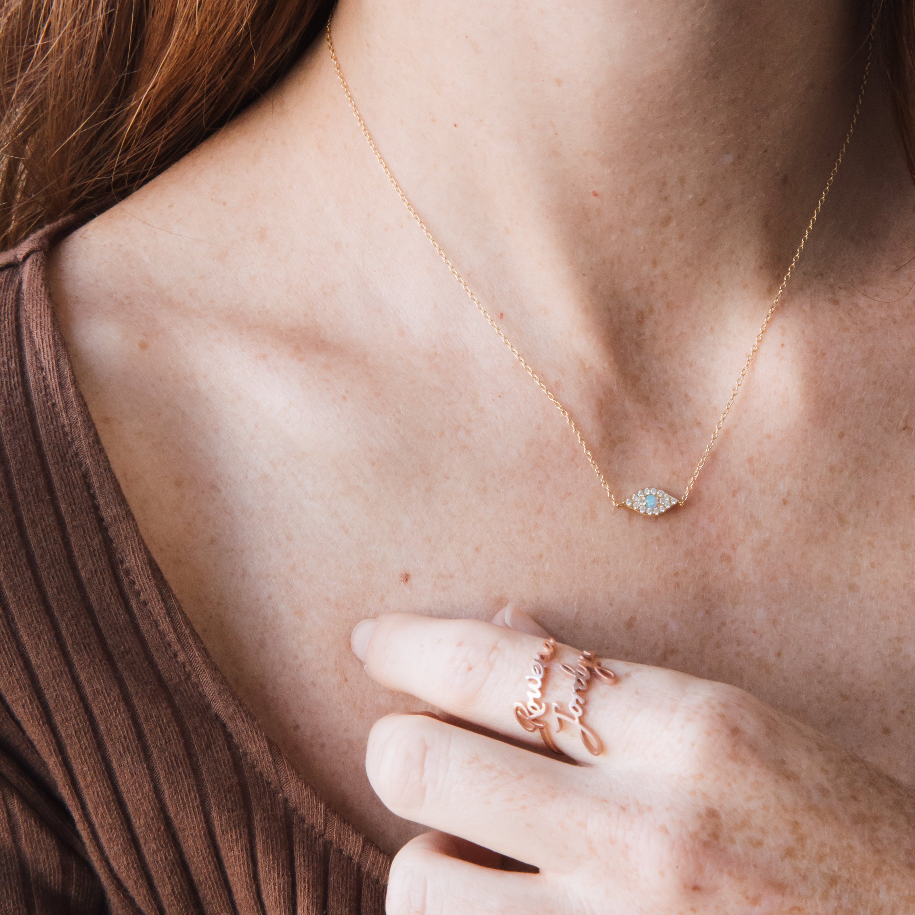 A woman wearing the Opal Eye Necklace with a small eye pendant and a 925 sterling silver forever family ring on her finger.