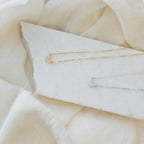 The Pave Heart Necklace, shown in gold and silver, rests on a white stone with a soft beige fabric background, highlighting its delicate and minimalist heart pendant design.