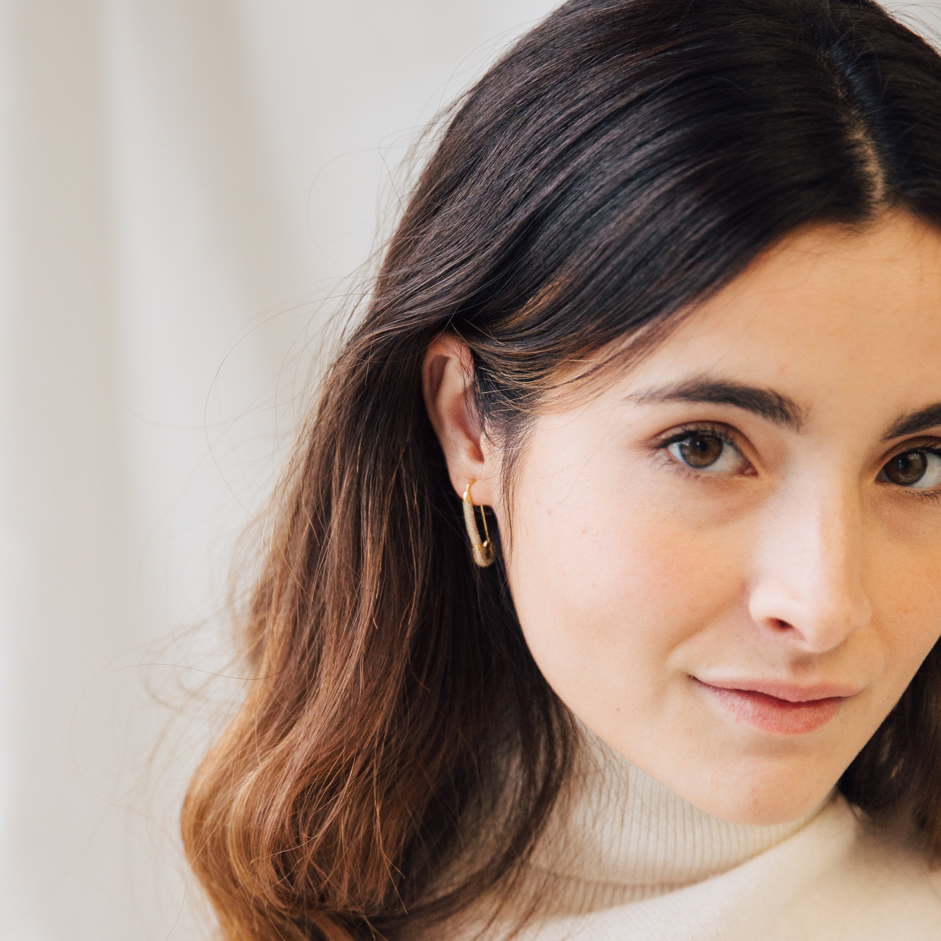 Woman with long brown hair, wearing a white turtleneck and Safety Pin Earrings Set, looking at the camera.