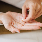 A person holds Stella Star Studs, small gold dainty earrings, in one hand and touches them with the other.