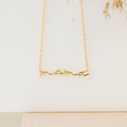 Gold necklace featuring the word “mama” in elegant cursive script, suspended from a delicate chain. Displayed against a clean, neutral background with soft lighting.