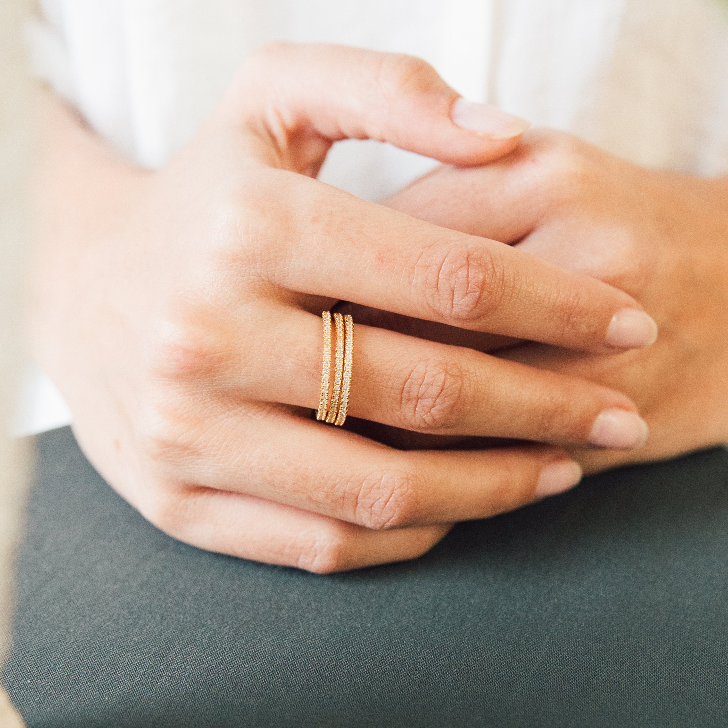 A hand with neatly manicured nails wears the Dove Eternity Ring, showcasing its elegant gold triple-band design and sparkling diamond-encrusted accents on the ring finger.