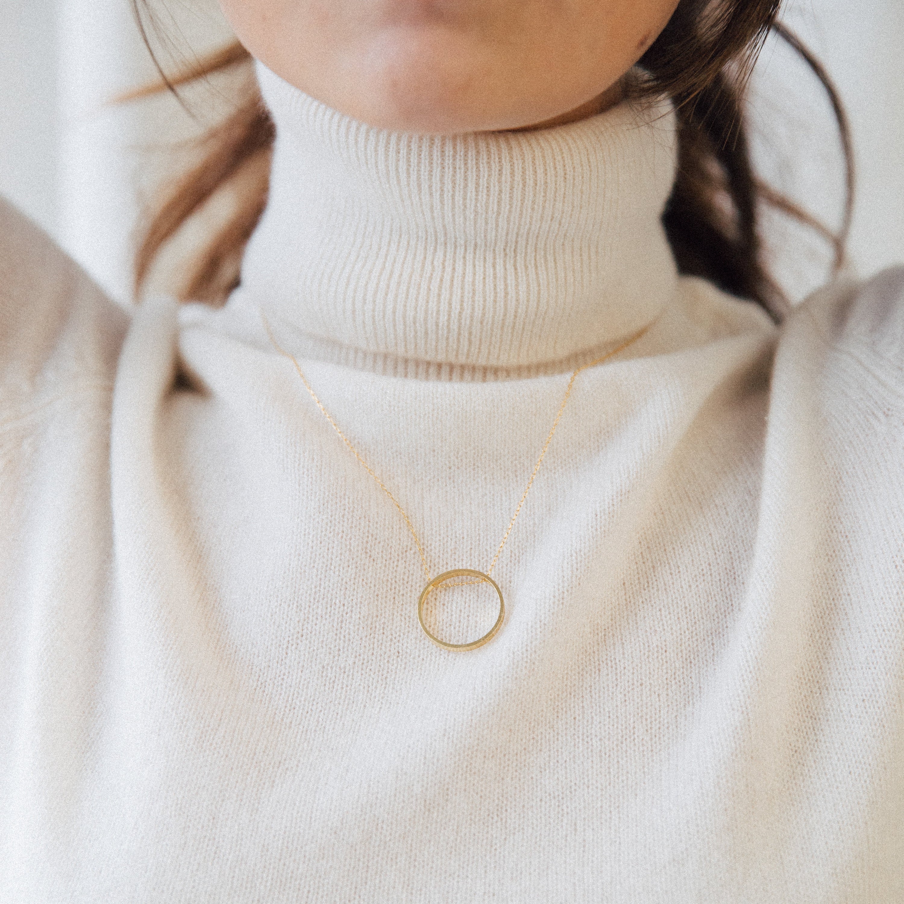 Woman in a cream turtleneck sweater wearing the Inner Circle Necklace in Rose Gold, a circle pendant and chain that adds effortless elegance.