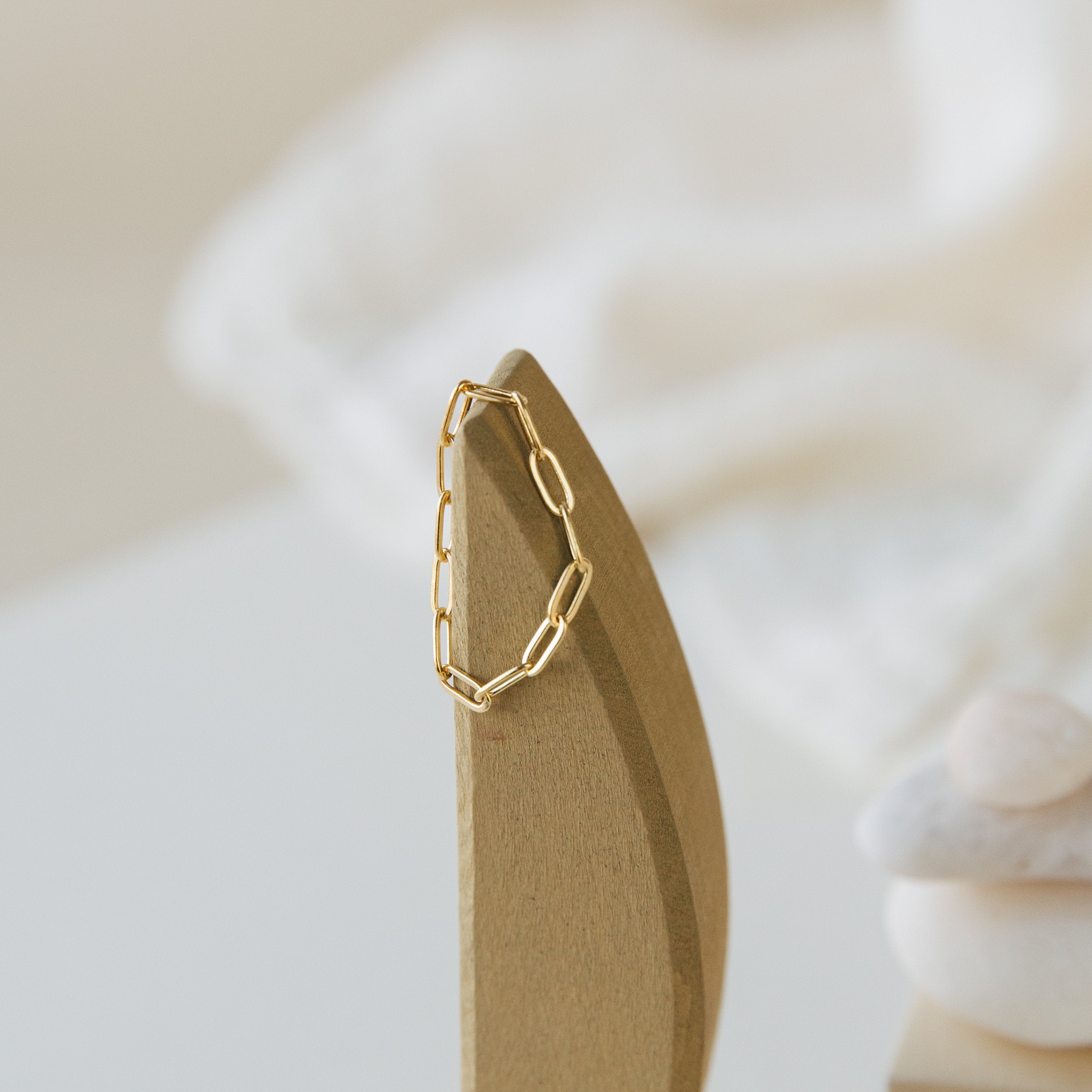 A gold chain link earring on a smooth wooden stand with a soft background—perfect to pair with our stylish Paperclip Chain Ring.