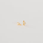 The Enya Huggies are small gold earrings, each with a star-shaped prong design and an iridescent diamond at the center.